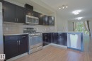 Kitchen featuring dark wood cabinetry, stainless steel appliances, light-toned countertops, subway tile backsplash, and wood-finish flooring - #13 5873 Mullen Pl Nw, Edmonton, AB  - Indoor Photo Showing Kitchen 
