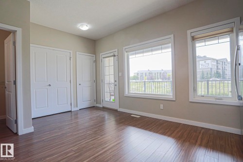 Wood-finish flooring, multiple windows providing natural illumination, and a glass-paned exterior door - #13 5873 Mullen Pl Nw, Edmonton, AB - Indoor Photo Showing Other Room