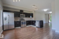 Kitchen featuring dark cabinetry, stainless steel appliances, an island with an undermount sink, a tiled backsplash, and wood-finish flooring - 