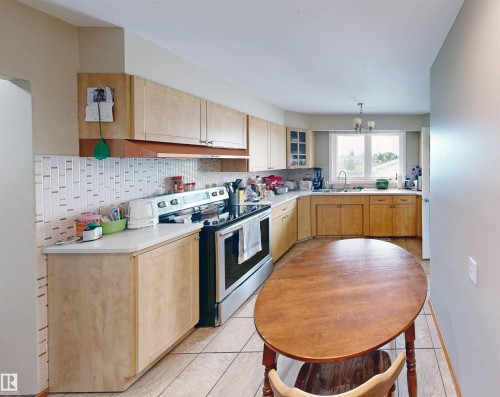 Kitchen featuring wood-finish cabinetry, white countertops, a mosaic tile backsplash, and stainless steel appliances - 9531 74 Street Nw, Edmonton, AB - Indoor Photo Showing Kitchen With Double Sink