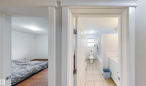 Wood-finish flooring in room, recessed ceiling light, white walls, light-toned floor tiling in bathroom, white vanity with integrated sink - 9531 74 Street Nw, Edmonton, AB - Indoor