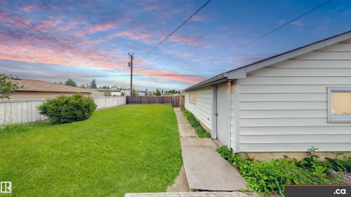 Expansive grassy yard area featuring a wooden fence, mature shrubbery, and a single-story outbuilding with horizontal siding and windows - 9531 74 Street Nw, Edmonton, AB - Outdoor