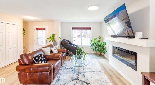 Open-concept living area featuring wood-finish flooring, a contemporary electric fireplace with a white mantel, and bright recessed lighting - 8527 Ellis Link Nw, Edmonton, AB - Indoor Photo Showing Living Room With Fireplace