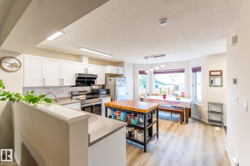 Kitchen featuring white cabinetry, stainless steel appliances, a tile backsplash, and wood-finish flooring - 8527 Ellis Link Nw, Edmonton, AB - Indoor Photo Showing Kitchen