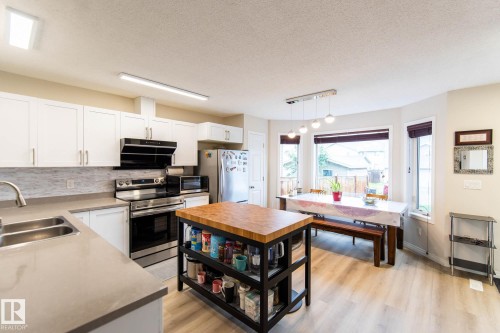 Kitchen featuring stainless steel appliances, white cabinetry, undermount double-basin sink, and a light-toned wood-finish flooring - 8527 Ellis Link Nw, Edmonton, AB - Indoor Photo Showing Kitchen With Double Sink