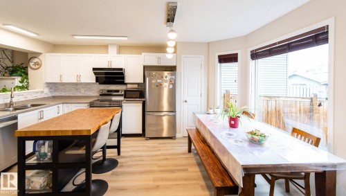 Kitchen featuring white cabinetry, stainless steel appliances, wood-finish flooring, a butcher block island, and large windows - 8527 Ellis Link Nw, Edmonton, AB - Indoor