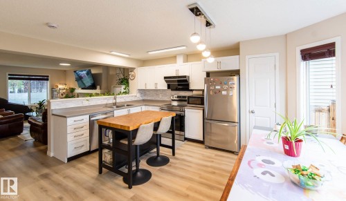 Open-concept kitchen featuring white cabinetry, stainless steel appliances, wood-finish flooring, and a breakfast bar island with a butcher block countertop - 8527 Ellis Link Nw, Edmonton, AB - Indoor Photo Showing Kitchen With Double Sink