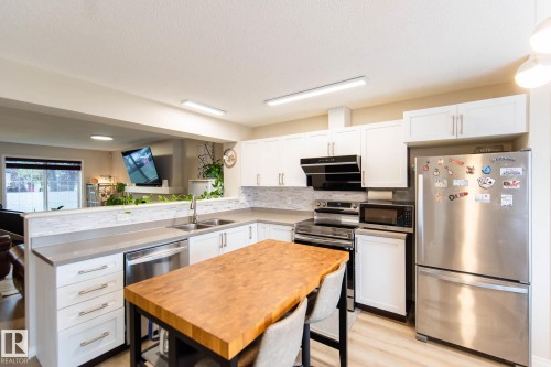 Modern kitchen featuring white shaker cabinetry, stainless steel appliances, light wood-finish flooring, and a butcher block island - 8527 Ellis Link Nw, Edmonton, AB - Indoor Photo Showing Kitchen With Double Sink