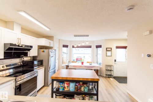 Kitchen featuring stainless steel appliances, white cabinetry with gold-tone hardware, wood-finish flooring, and a bay window - 8527 Ellis Link Nw, Edmonton, AB - Indoor Photo Showing Kitchen