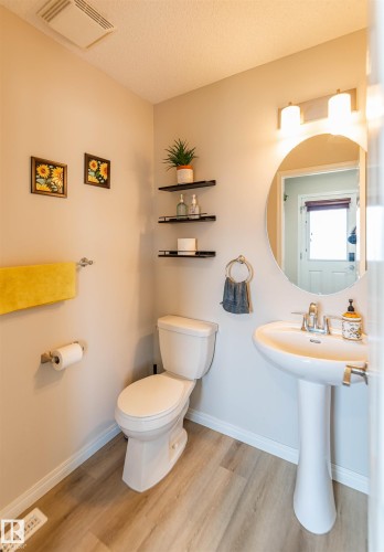 Pedestal sink with chrome fixtures, wood-finish flooring, wall-mounted oval mirror, and three-light vanity bar - 8527 Ellis Link Nw, Edmonton, AB - Indoor Photo Showing Bathroom