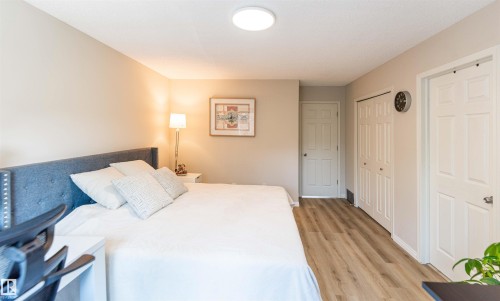 Spacious room featuring wood-finish flooring, light neutral wall paint, a flush-mount ceiling light fixture, and multiple panel doors - 8527 Ellis Link Nw, Edmonton, AB - Indoor Photo Showing Bedroom