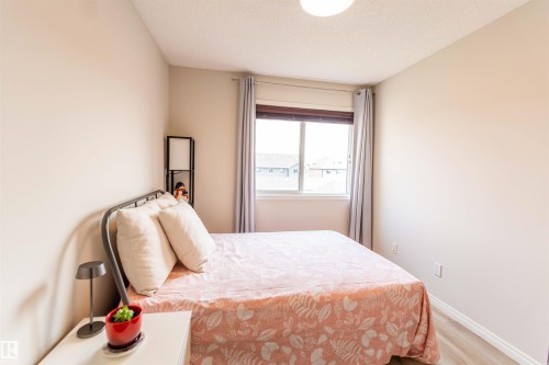 Bedroom featuring a large window with blinds, light wood-finish flooring, neutral wall tones, and a ceiling-mounted light fixture - 8527 Ellis Link Nw, Edmonton, AB - Indoor Photo Showing Bedroom