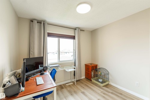 Light-filled room featuring wood-finish flooring, a contemporary flush-mount ceiling light, and a large window with privacy blinds and drapes - 8527 Ellis Link Nw, Edmonton, AB - Indoor