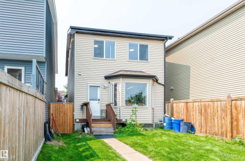 Rear exterior featuring beige siding, a bay window, and a ground-level deck with wooden steps - 8527 Ellis Link Nw, Edmonton, AB - Outdoor