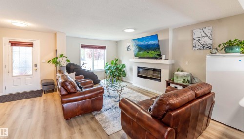 Spacious living area featuring wood-finish flooring, a contemporary electric fireplace with a floating mantel, and a front entry door with decorative glass - 8527 Ellis Link Nw, Edmonton, AB - Indoor Photo Showing Living Room With Fireplace