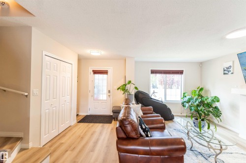 Open-concept living area with light-toned wood-finish flooring, a white front entry door with privacy glass, a window with horizontal blinds, and a built-in closet with bifold doors - 8527 Ellis Link Nw, Edmonton, AB - Indoor Photo Showing Living Room