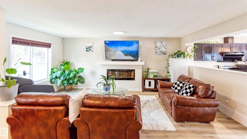 Open-concept living area featuring light wood-finish flooring, a built-in electric fireplace with a white mantel, an expansive window, and recessed lighting - 8527 Ellis Link Nw, Edmonton, AB - Indoor Photo Showing Living Room With Fireplace