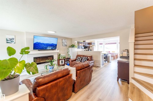 Open concept living space featuring wood-finish flooring throughout, a white mantel with a linear electric fireplace, and a partial wall separating the kitchen area - 8527 Ellis Link Nw, Edmonton, AB - Indoor Photo Showing Living Room With Fireplace