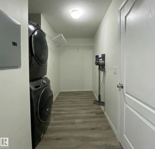 This laundry area features a stacked washer and dryer, a wire shelf, and light-toned flooring - #6125 7331 South Terwillegar Dr Nw, Edmonton, AB - Indoor Photo Showing Laundry Room