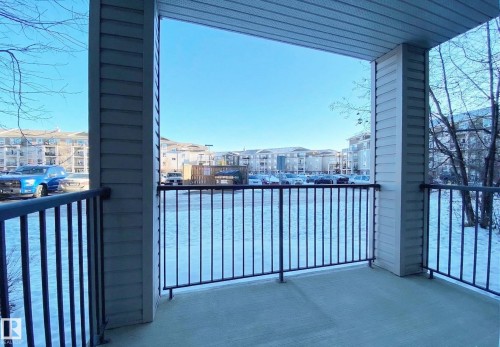 The property features a balcony with a concrete floor and black metal railings, offering views of the surrounding neighborhood buildings and parking areas - #6125 7331 South Terwillegar Dr Nw, Edmonton, AB - Outdoor