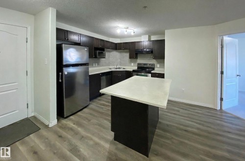 The property features a kitchen with dark cabinetry, stainless steel appliances, a light-colored countertop, and an island - #6125 7331 South Terwillegar Dr Nw, Edmonton, AB - Indoor Photo Showing Kitchen With Double Sink