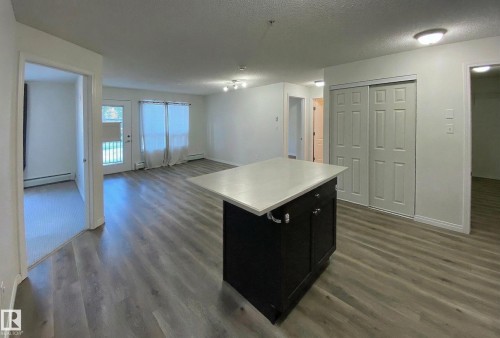 Open concept living area with hardwood style flooring, a kitchen island with a light-colored countertop, and a sliding door leading to an outdoor space - #6125 7331 South Terwillegar Dr Nw, Edmonton, AB - Indoor