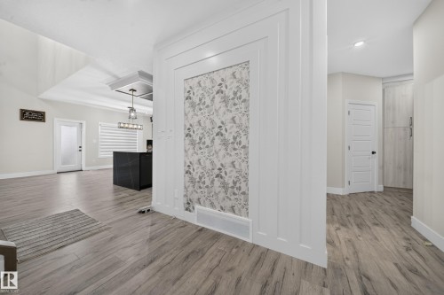 Wood-finish flooring throughout, featuring a decorative wall panel with botanical wallpaper insert - 3217 Pelerin Crescent, Beaumont, AB - Indoor Photo Showing Other Room