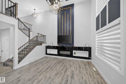 Two-story ceiling, wood-finish flooring, staircase with dark wood-finish handrails and black balusters, built-in black marble-finish media console with open shelving, and a wall-mounted decorative accent panel - 3217 Pelerin Crescent, Beaumont, AB - Indoor Photo Showing Other Room