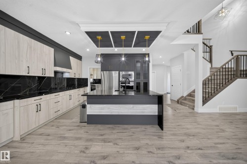 Modern kitchen featuring light wood-finish cabinetry with black hardware, black countertops, and a full-height black backsplash - 3217 Pelerin Crescent, Beaumont, AB - Indoor