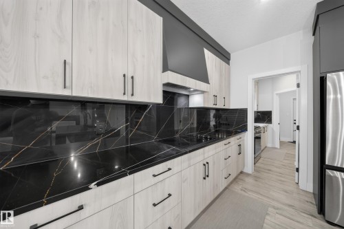 Contemporary kitchen featuring light wood-finish cabinetry, black countertops with white and gold veining, a matching backsplash, and a stainless steel refrigerator - 3217 Pelerin Crescent, Beaumont, AB - Indoor Photo Showing Kitchen