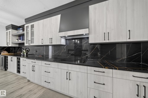 Light wood-finish cabinetry with matte black hardware, black countertops with white and gold veining, matching black backsplash, built-in wine storage, and a range hood with integrated lighting - 3217 Pelerin Crescent, Beaumont, AB - Indoor Photo Showing Other Room