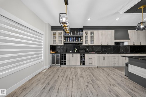 Wood-finish flooring, full-height black marble-patterned backsplash, light wood-tone cabinetry, built-in wine storage, and a modern rectangular chandelier - 3217 Pelerin Crescent, Beaumont, AB - Indoor Photo Showing Kitchen