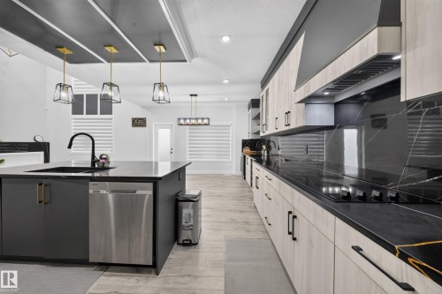 Contemporary kitchen featuring a large central island, black stone countertops with veining, light wood-finish cabinetry, built-in stainless steel dishwasher, and modern pendant lighting - 3217 Pelerin Crescent, Beaumont, AB - Indoor Photo Showing Kitchen With Upgraded Kitchen