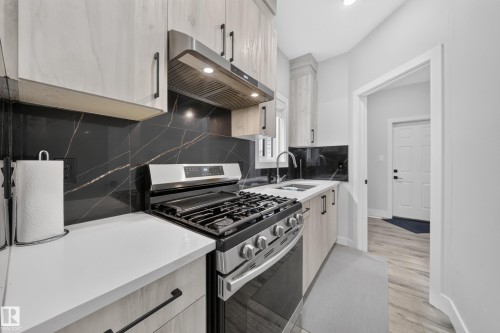 Stainless steel gas range, black and white veined backsplash, light wood-finish cabinetry, light-toned countertops, and recessed lighting - 3217 Pelerin Crescent, Beaumont, AB - Indoor Photo Showing Kitchen