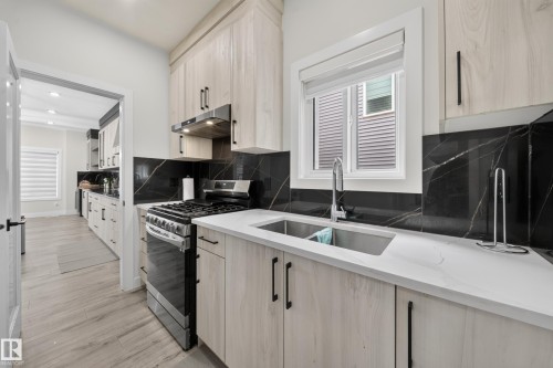 Contemporary kitchen featuring light wood-finish cabinetry, white countertops, and a black stone-finish backsplash - 3217 Pelerin Crescent, Beaumont, AB - Indoor Photo Showing Kitchen