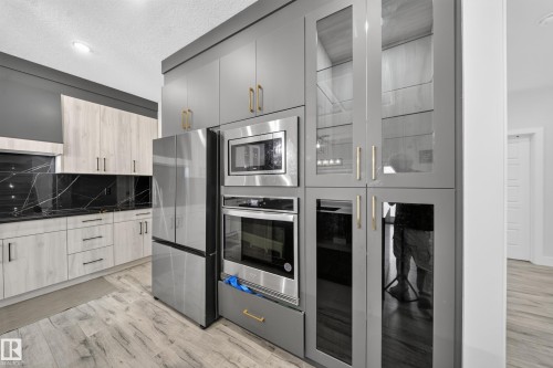 Modern kitchen featuring stainless steel appliances, light wood-finish cabinetry, black countertops with a matching backsplash, and wood-finish flooring - 3217 Pelerin Crescent, Beaumont, AB - Indoor Photo Showing Kitchen