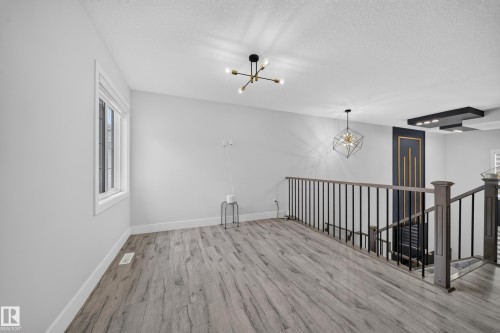 Wood-finish flooring, white walls, modern ceiling light fixture, window with white trim, and a black and wood staircase railing - 3217 Pelerin Crescent, Beaumont, AB - Indoor Photo Showing Other Room