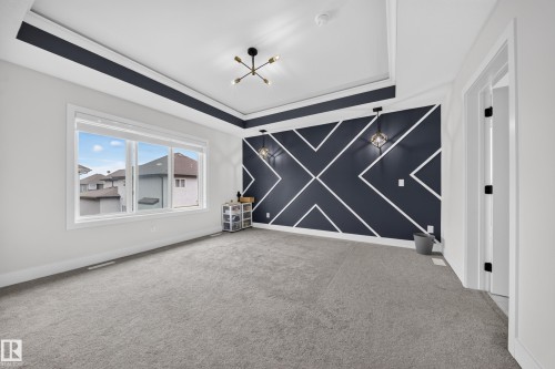 Tray ceiling with dark accent trim, modern chandelier, accent wall with geometric design, wall-mounted sconces, and light gray carpeting - 3217 Pelerin Crescent, Beaumont, AB - Indoor Photo Showing Other Room