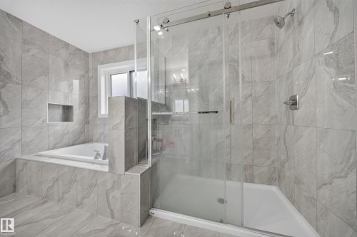 Modern bathroom featuring large format gray tile, a spacious walk-in shower with clear glass enclosure and sliding door, a built-in soaking tub, and a window for natural illumination - 3217 Pelerin Crescent, Beaumont, AB - Indoor Photo Showing Bathroom