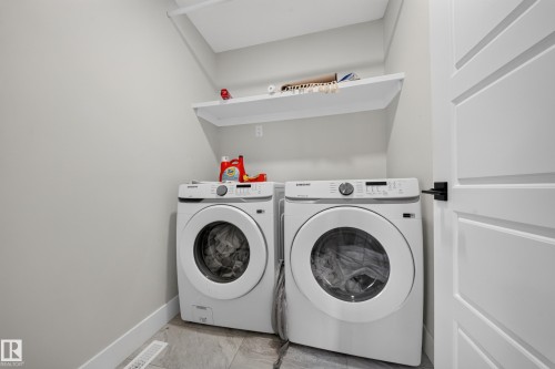 Functional laundry area featuring a built-in shelf, light gray walls, and gray tile flooring - 3217 Pelerin Crescent, Beaumont, AB - Indoor Photo Showing Laundry Room