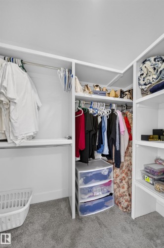 Walk-in closet featuring dual clothing rods with hanging space, built-in shelving with storage bins, a laundry hamper, and gray tile flooring throughout - 3217 Pelerin Crescent, Beaumont, AB - Indoor With Storage