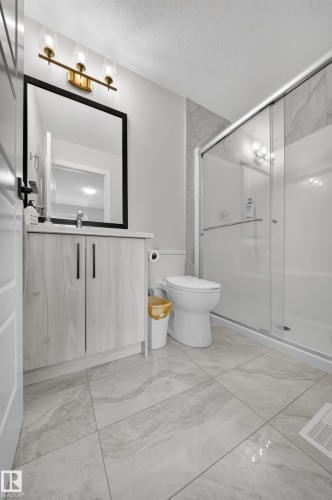 Light wood-finish vanity with dark hardware, framed mirror, and three-light vanity fixture - 3217 Pelerin Crescent, Beaumont, AB - Indoor Photo Showing Bathroom