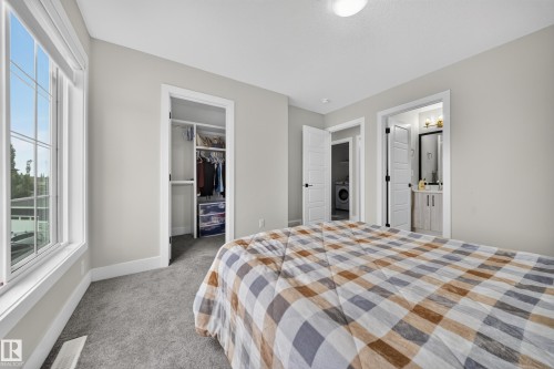 Carpeted room featuring a window with grid patterns, a built-in closet, and access to an adjoining room with a vanity and mirror - 3217 Pelerin Crescent, Beaumont, AB - Indoor Photo Showing Bedroom