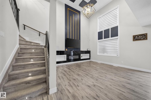 Open-concept living space with wood-finish flooring, a contemporary built-in media console, and a unique accent wall with vertical gold-toned detailing - 3217 Pelerin Crescent, Beaumont, AB - Indoor Photo Showing Other Room