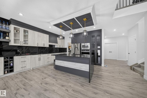 Expansive kitchen featuring a large central island, black countertops, integrated stainless steel appliances, and wood-finish flooring - 3217 Pelerin Crescent, Beaumont, AB - Indoor