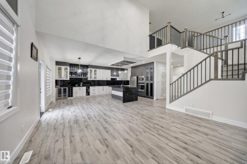 Vaulted ceiling, wood-finish flooring, staircase with metal spindles, two-tone kitchen cabinetry, and a kitchen island with a dark countertop - 3217 Pelerin Crescent, Beaumont, AB - Indoor Photo Showing Other Room