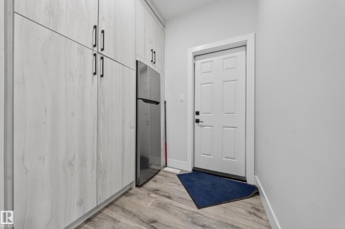Integrated refrigerator with full-height pantry cabinetry featuring matte black hardware, wood-finish flooring, and a paneled entry door - 3217 Pelerin Crescent, Beaumont, AB - Indoor Photo Showing Other Room