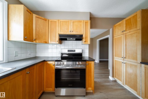 Wood-finish cabinetry, stainless steel range, white tile backsplash, dark countertops, and wood-finish flooring - 115 Griesbach Road Nw, Edmonton, AB - Indoor Photo Showing Kitchen