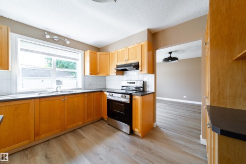 Wood-finish cabinetry, stainless steel range, white subway tile backsplash, dark countertops, and wood-finish flooring - 115 Griesbach Road Nw, Edmonton, AB - Indoor Photo Showing Kitchen