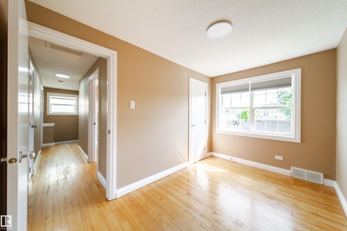 Bright corner bedroom with warm wood-finish flooring, generous natural light from dual windows, white trim detailing, and access to hallway and adjoining spaces - 115 Griesbach Road Nw, Edmonton, AB - Indoor Photo Showing Other Room